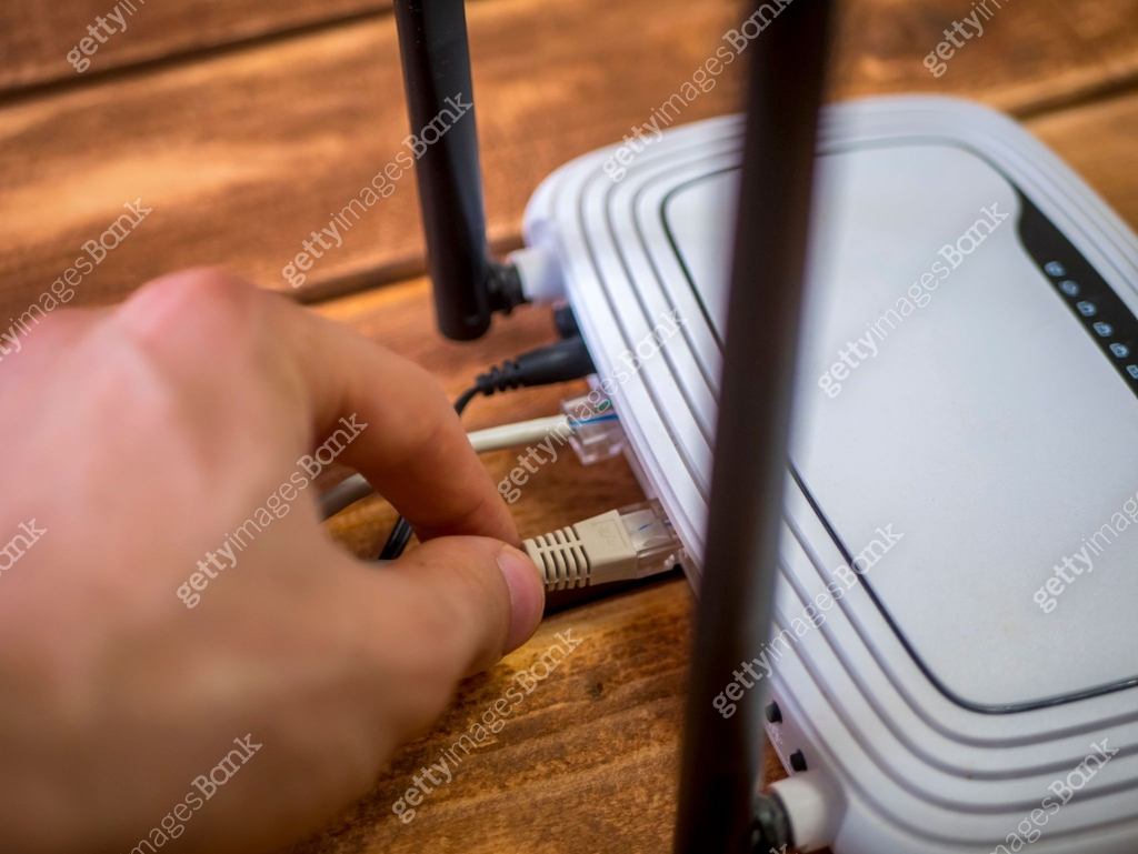 close up hand inserting ethernet wire in wi-fi router on wooden table ...