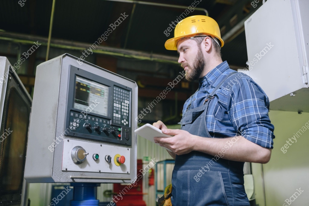 Serious professional bearded machine operator in hardhat looking at cnc ...