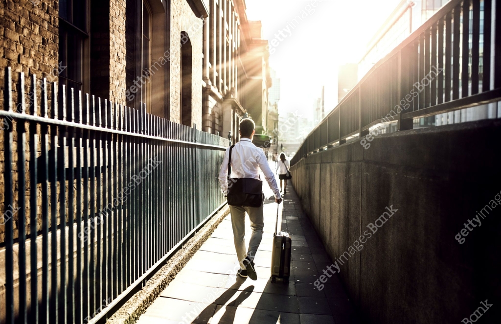 Rear view of businessman with suitcase walking up the street in London ...