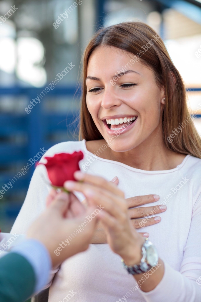Smiling young woman receiving a single red rose from her boyfriend or ...