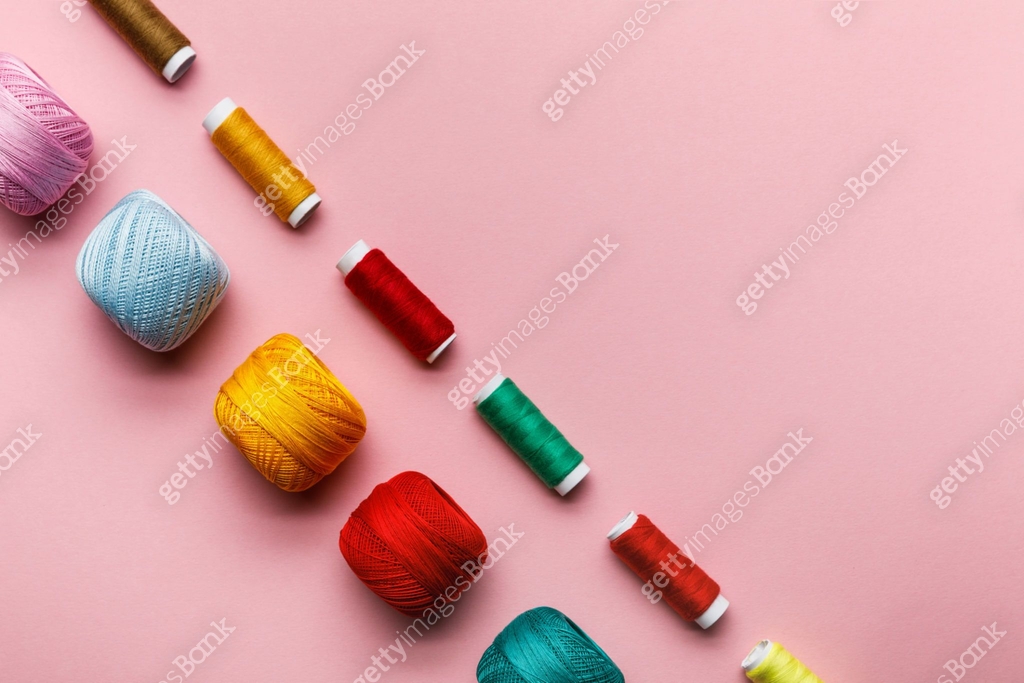top view of colorful knitting yarn balls and thread coils on pink with ...