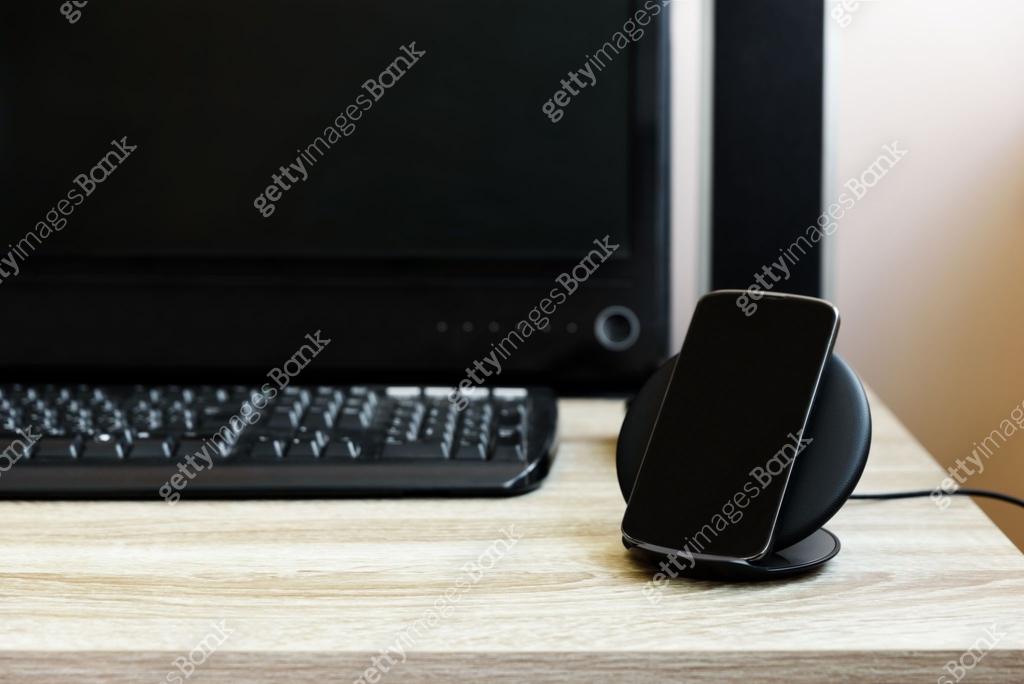 Black smartphone charged by wireless charger against computer monitor ...