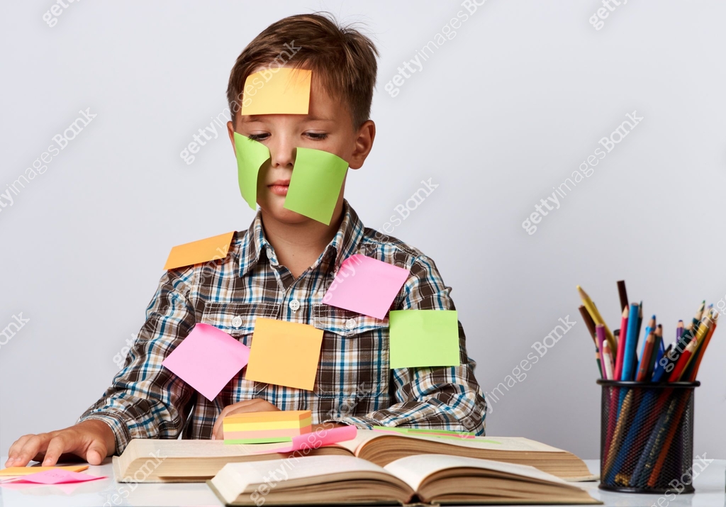 Tired boy with sticky notes on his face, sitting at desk and doing ...