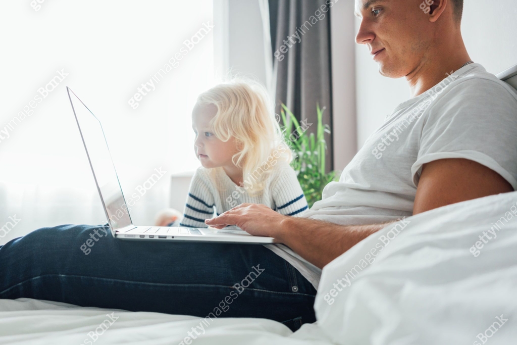 Young dad sits on bed with children using the computer together at home ...