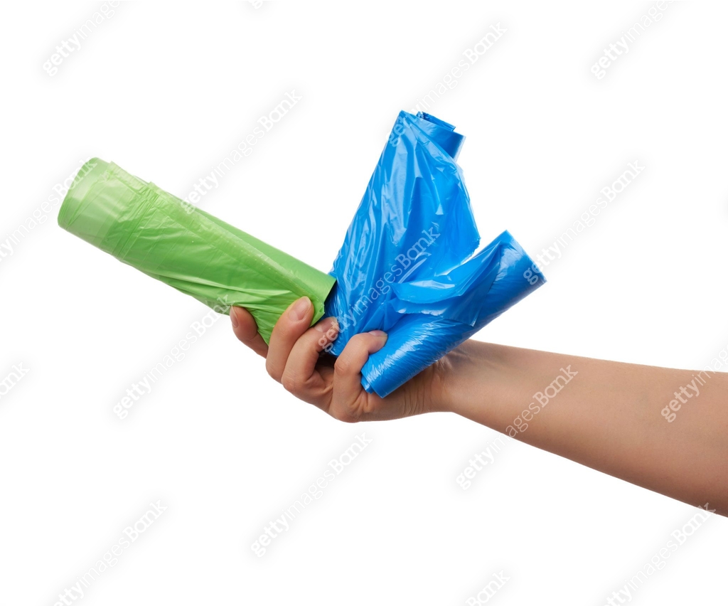 female hand holds a bundle of green and blue plastic bags for garbage ...