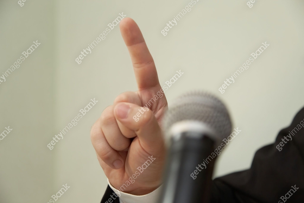 Close-up of an index finger raised upwards in front of a microphone ...