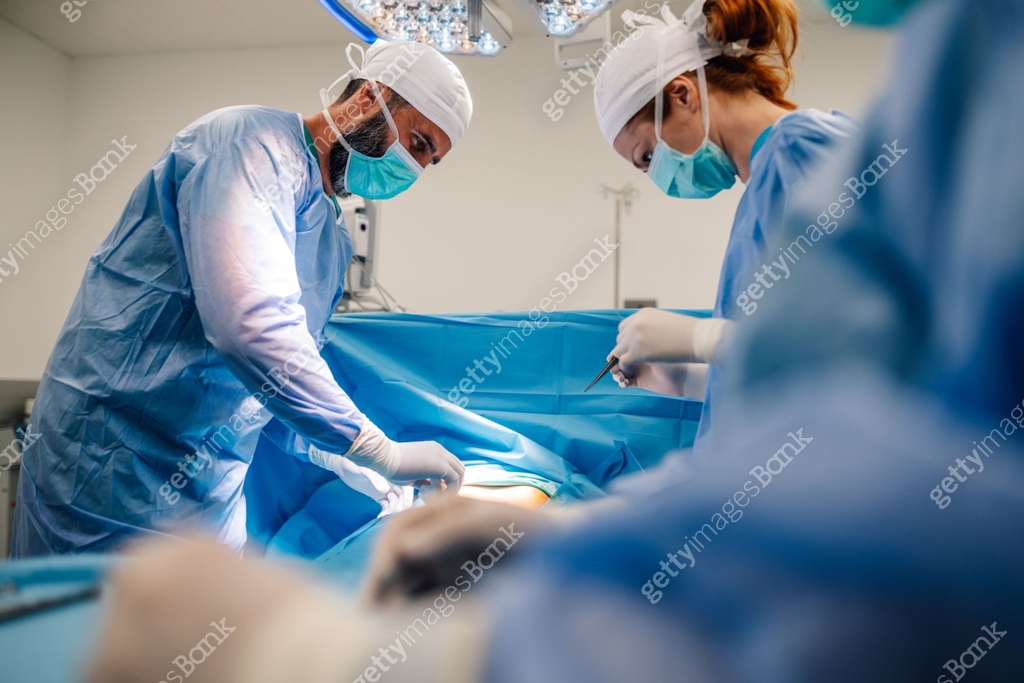 Surgical team performing operation in brightly lit, sterile environment ...