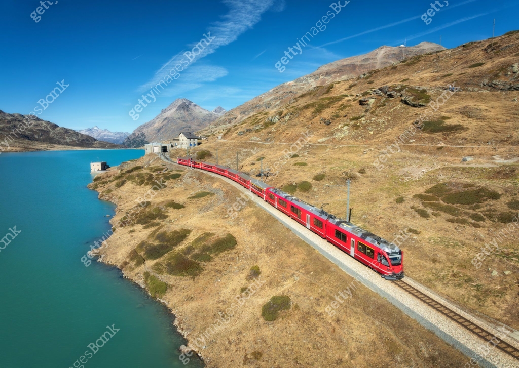 Azure Train Line Aerial view of modern red train near azure mountain lake, rocks and ...