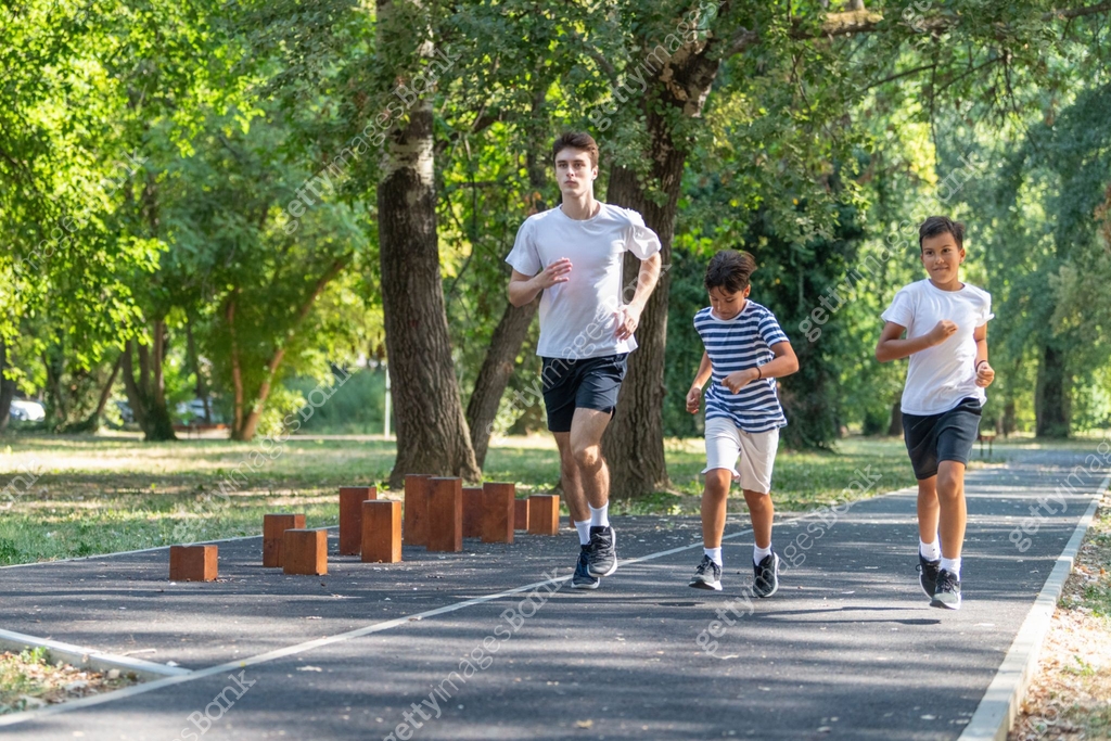 Learning Community Runing Trainer runs alongside two boys in a sunny park, focusing on improving ...
