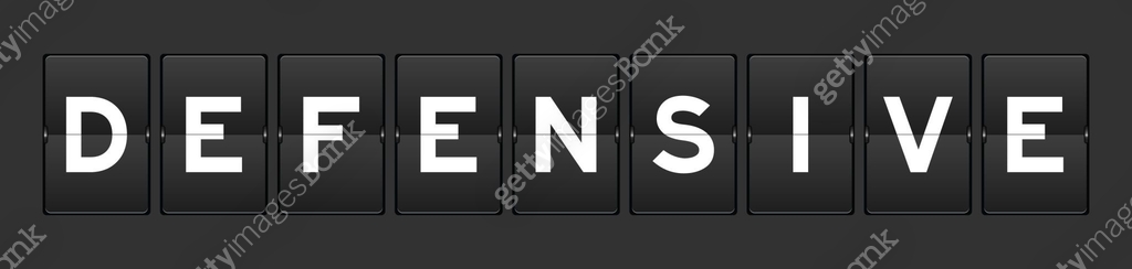 Black color analog flip board with word defensive on gray background ...