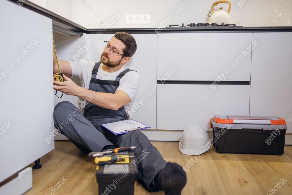 Handyman fixing kitchen cabinets in the apartment, measuring dimensions ...