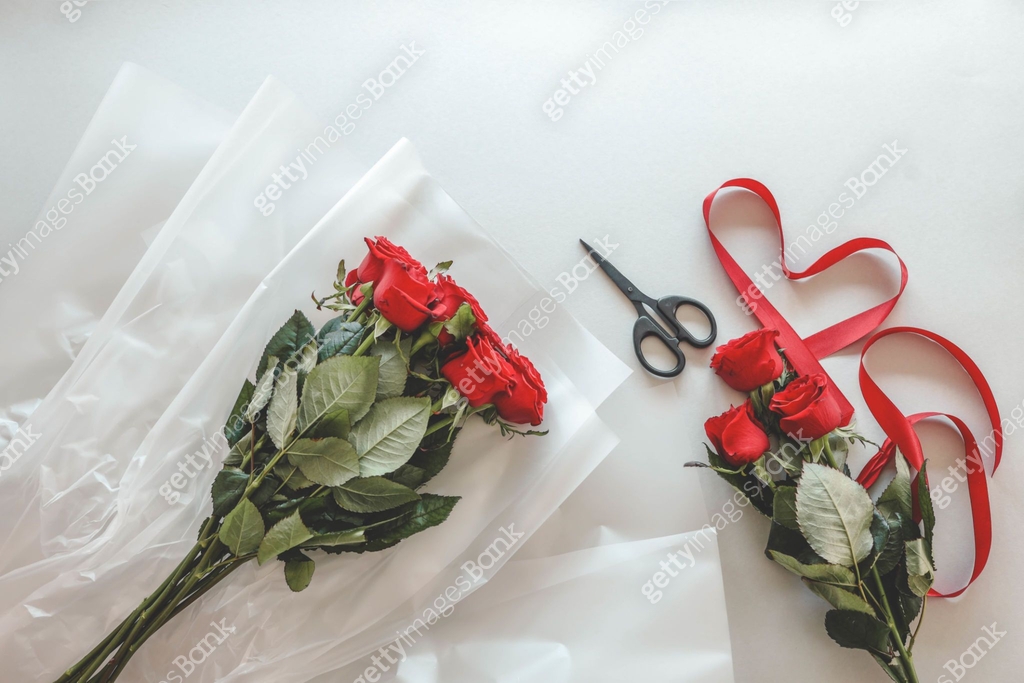Preparation of a bouquet with red roses, scissors, and ribbon on a ...