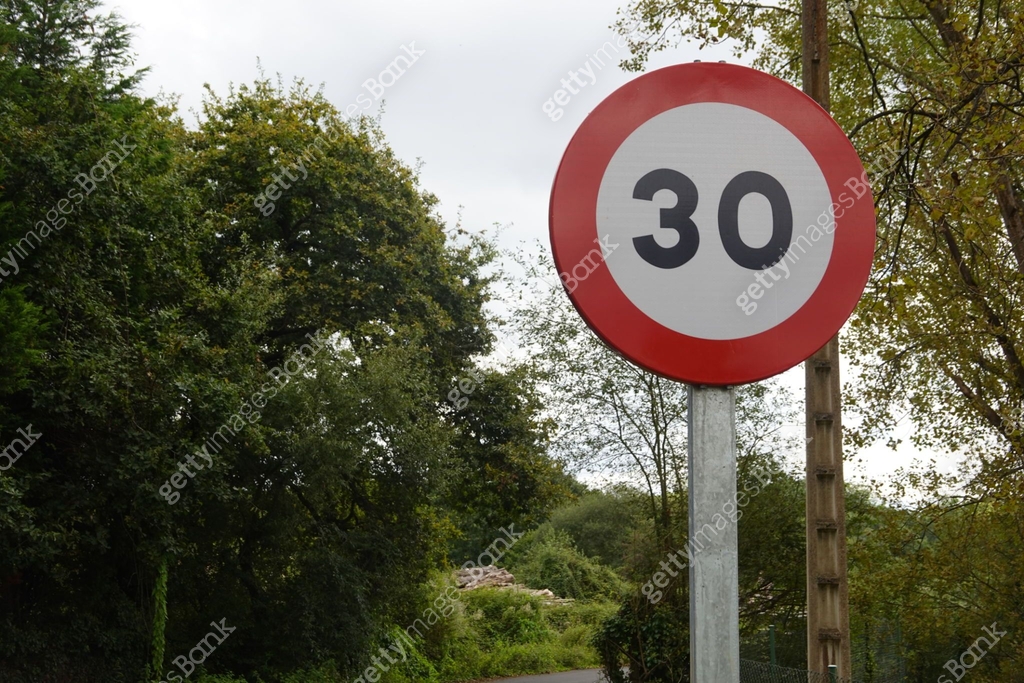 A speed limit sign showing 30 stands on a rural road bordered by thick ...