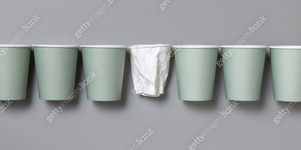 New light green paper cups and crumpled used white one on a gray top ...