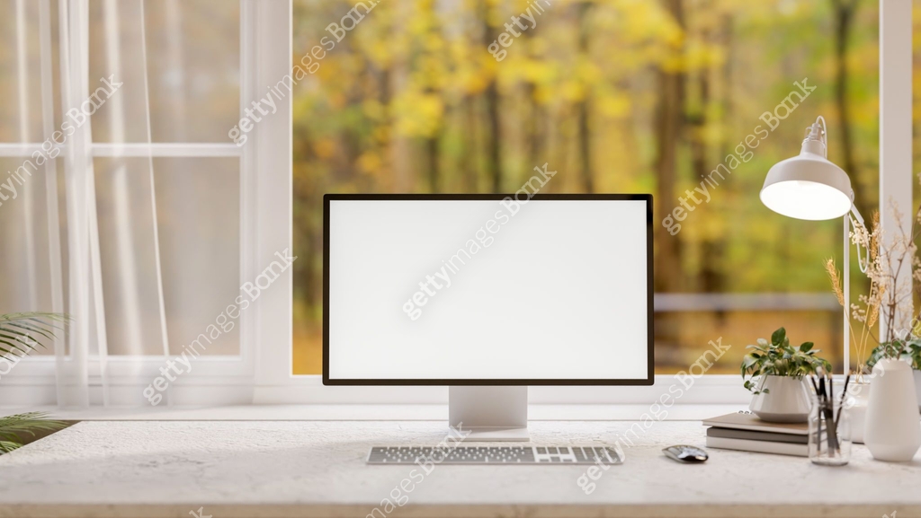 A front view of a computer on a desk, set against a window overlooking ...