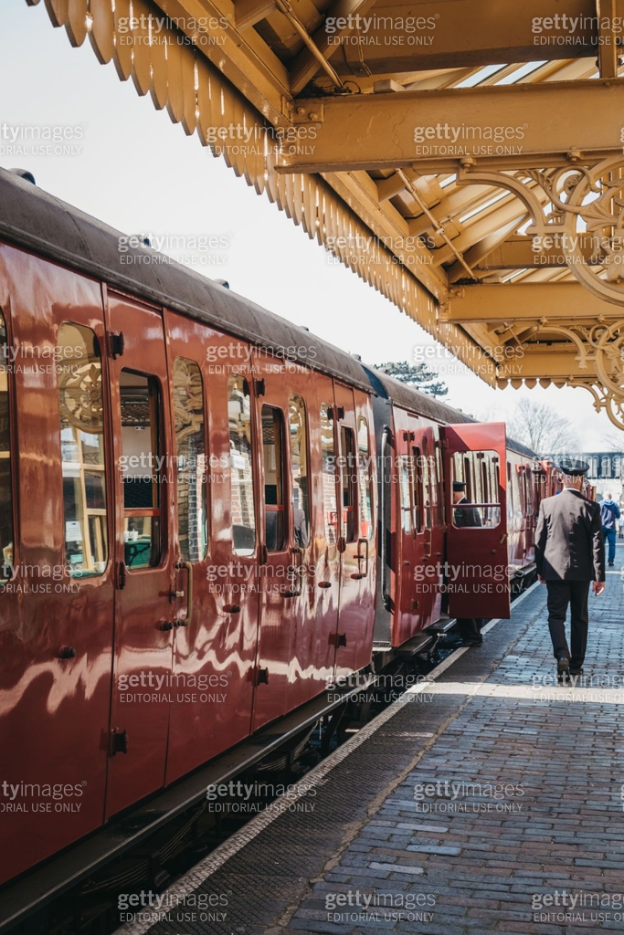 Poppy Train Conductor in uniform walking past a retro Poppy Line steam train at ...