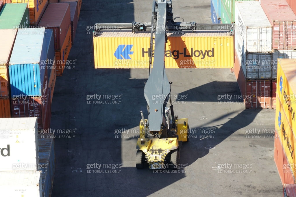 Reach stacker of yellow colour with orange container attached to black ...