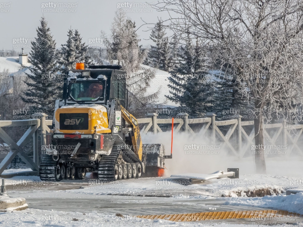 A yellow ASV RT-30 compact track loader clears snow from a path, its ...