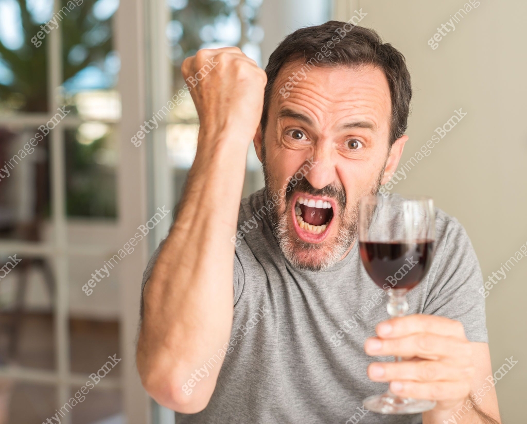 Middle age man drinking a glass of wine annoyed and frustrated shouting ...