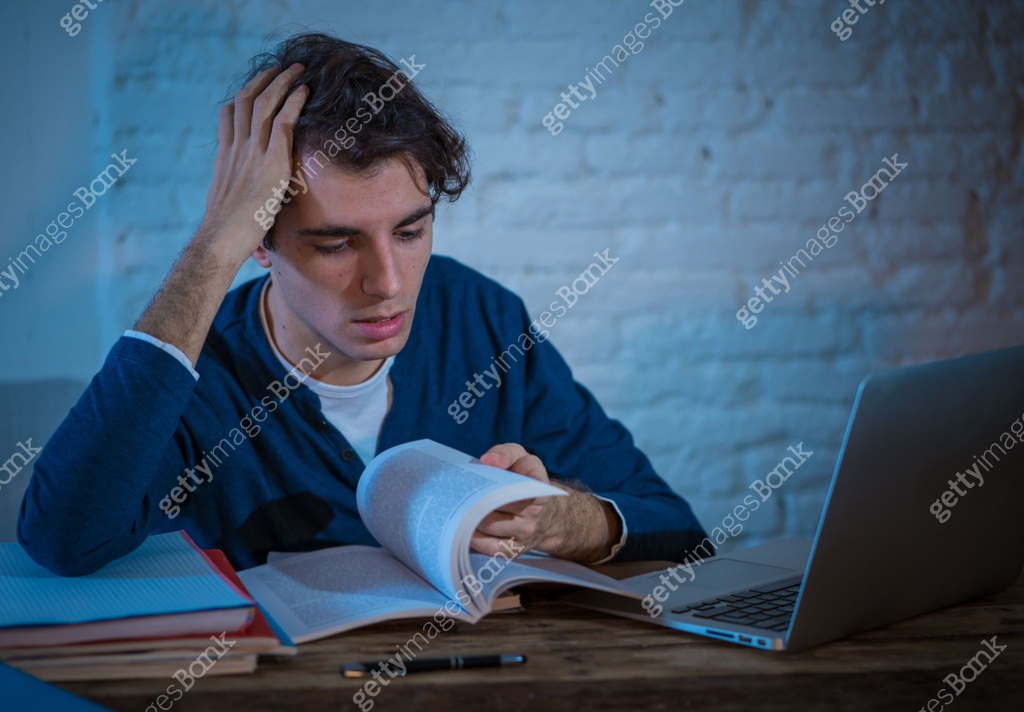 Overworked and tired male student working late at night on laptop ...