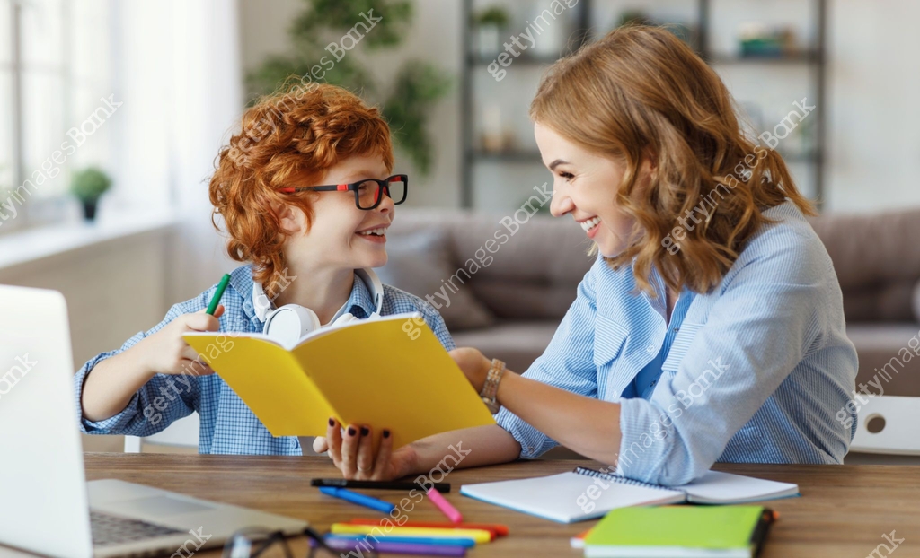 Mother helping child with homework, looks at her son's notebook at home ...