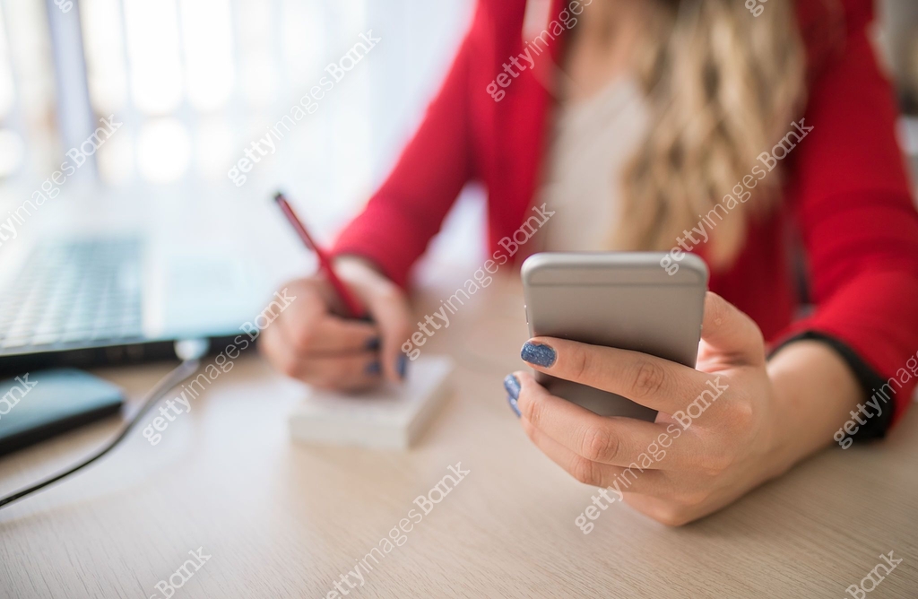 Writing Note On Phone Close up of a woman holding smartphone and writing notes at the office ...