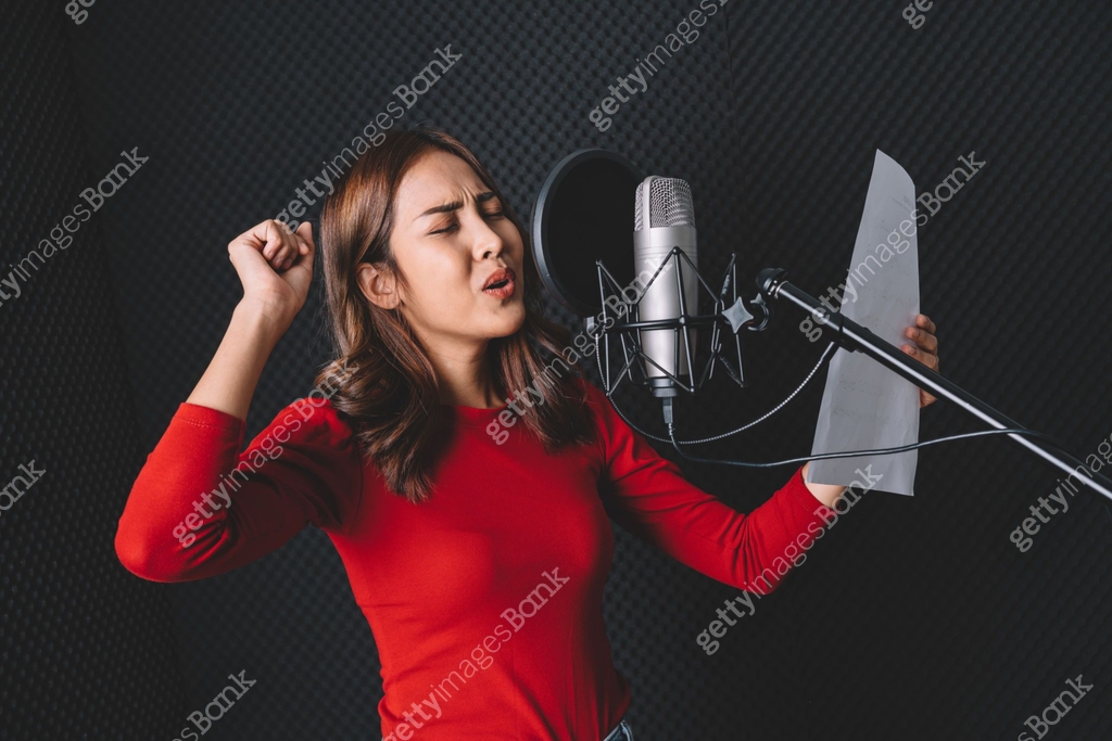 Pretty Asian female singer recording songs by using a studio microphone ...