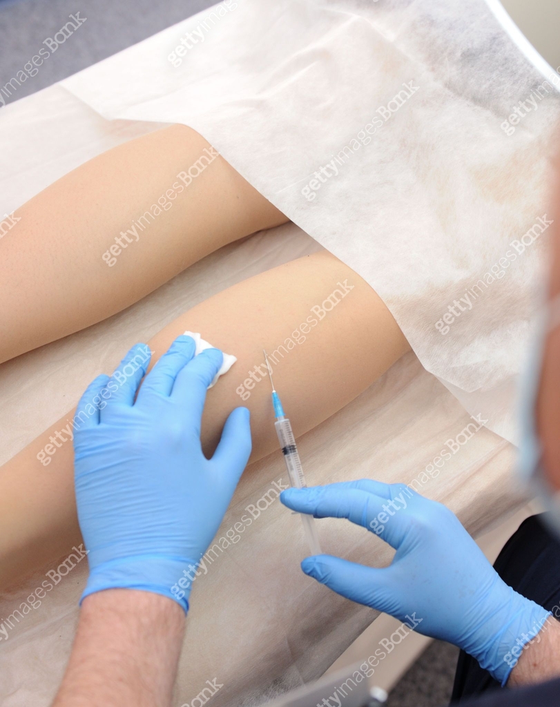 The doctor injects a syringe under the knee. A doctor makes an ...
