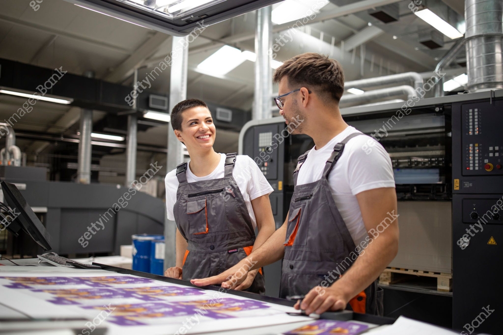 Printing machine operators checking graphic quality and color values at ...