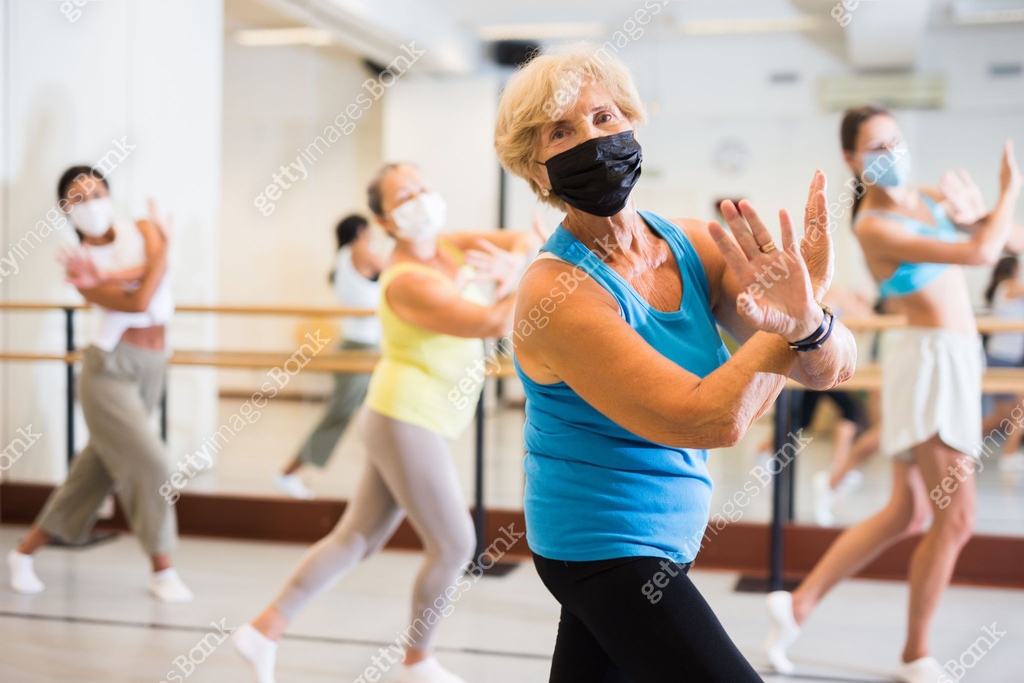 Women in protective mask practicing vigorous dance movements in group ...