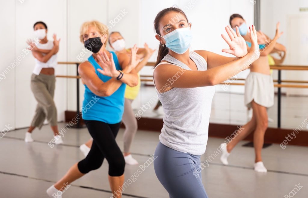 Women in protective mask practicing vigorous dance movements in group ...