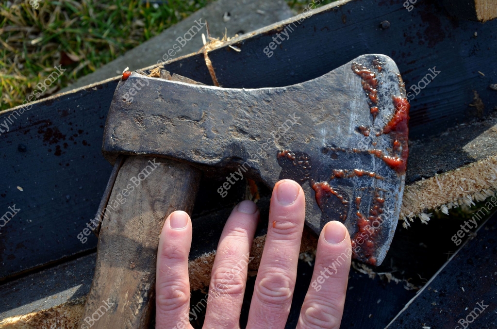 a bloody ax stuck in a log for chopping wood. a man in green pants and ...