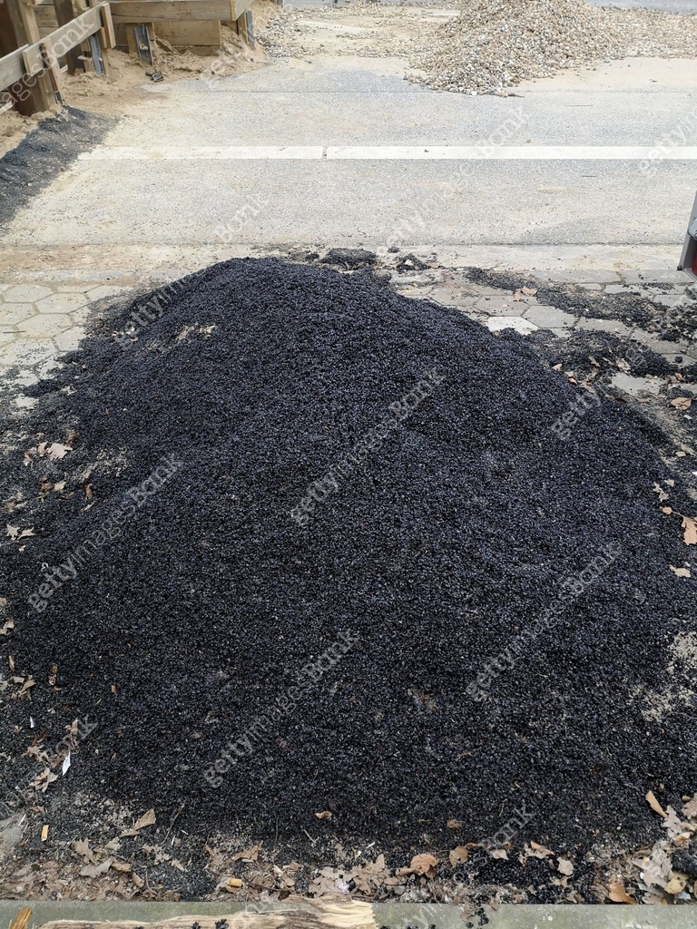 A pile of black, granular asphalt mixture. Material for repairing a ...