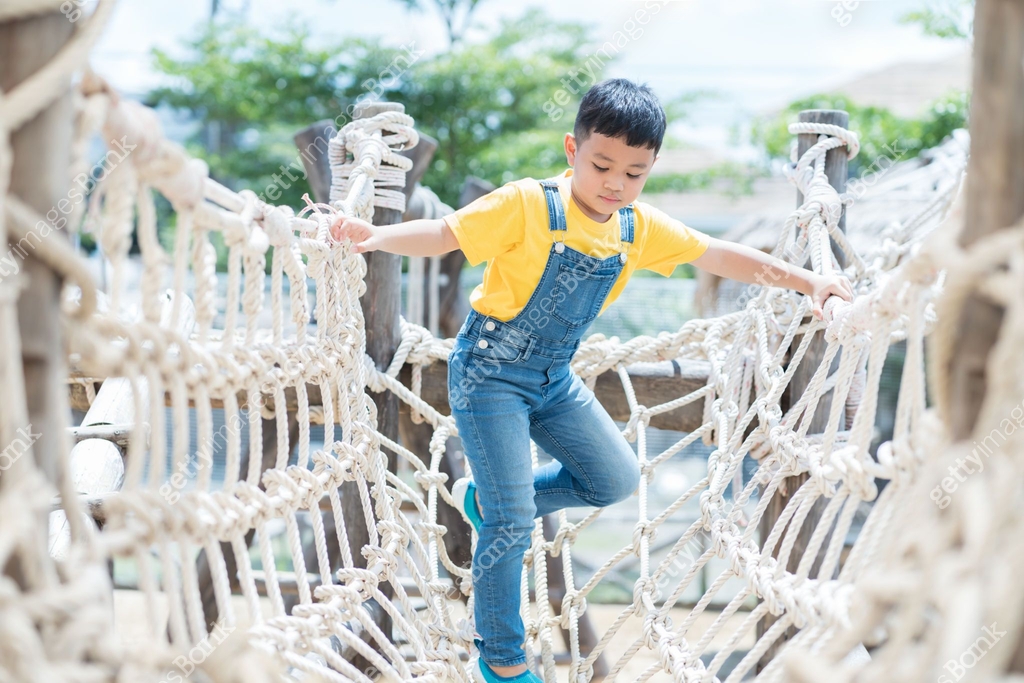 Boy Using A Rope Portrait of little boy playing on rope net bridge at the playground ...