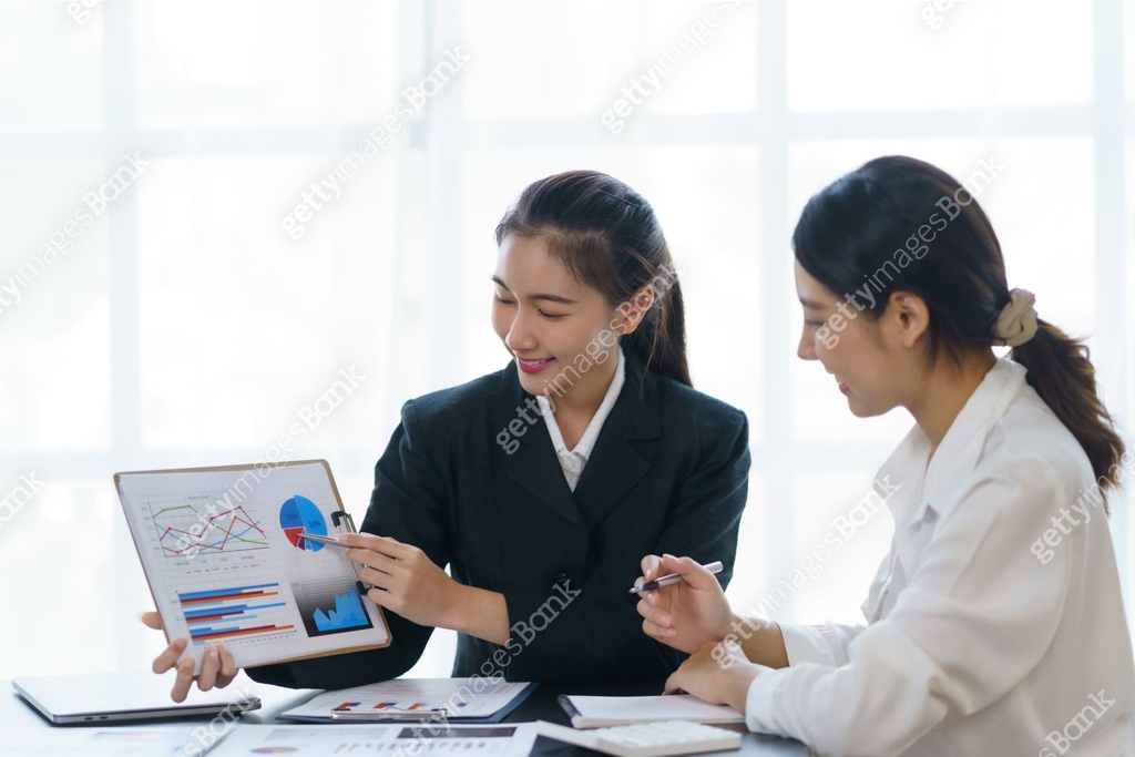 Two professional young Asian business women discuss work, graph, chart ...