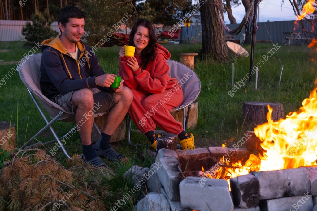 Banked Campire Couple in love is sitting by the outdoor campfire in the courtyard of ...