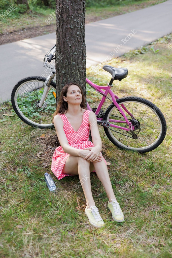 young female rides bicycle and sits resting on the lawn in the park by ...