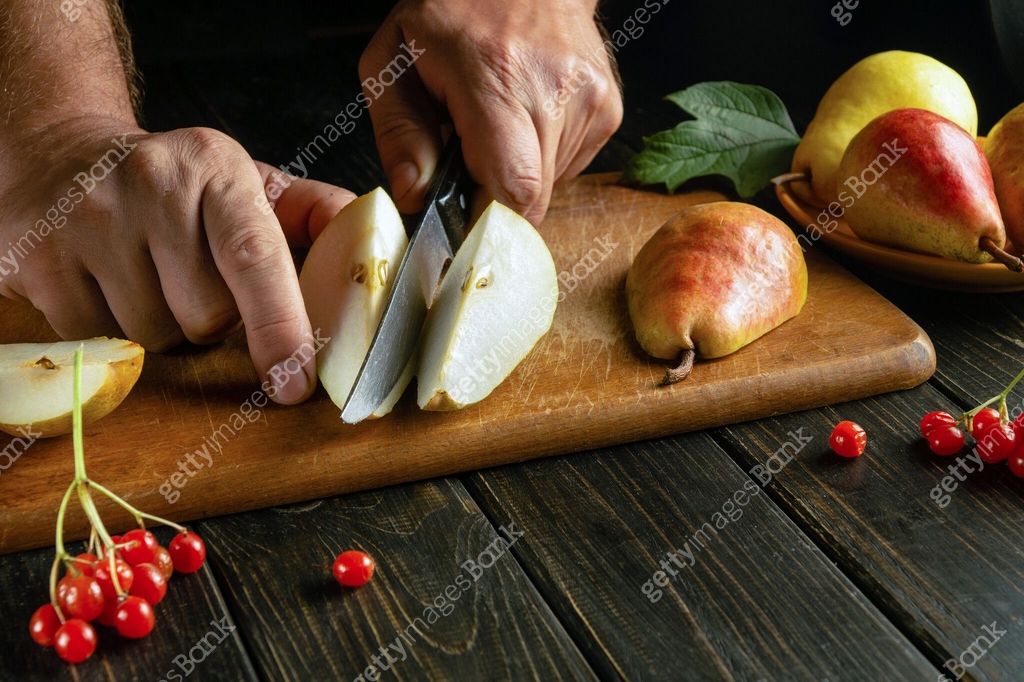 Pear Chef The chef cuts a pear with a knife on a cutting board to prepare compote ...