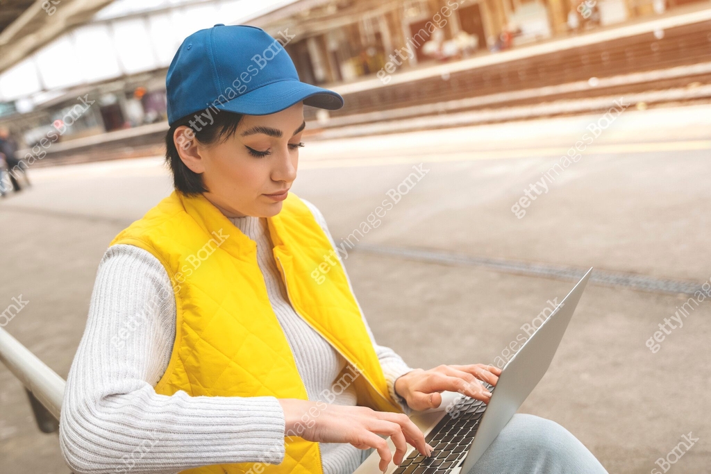 woman at railway station using computer, laptop while waiting train ...