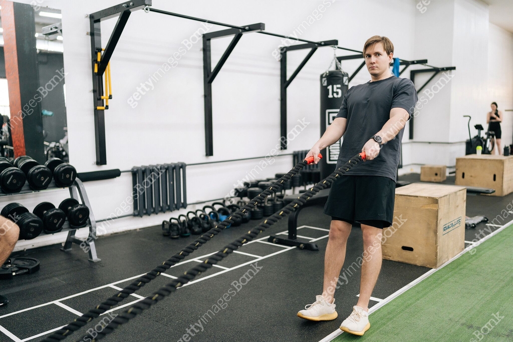 Portrait of beginner sportsman doing battle ropes functional training ...