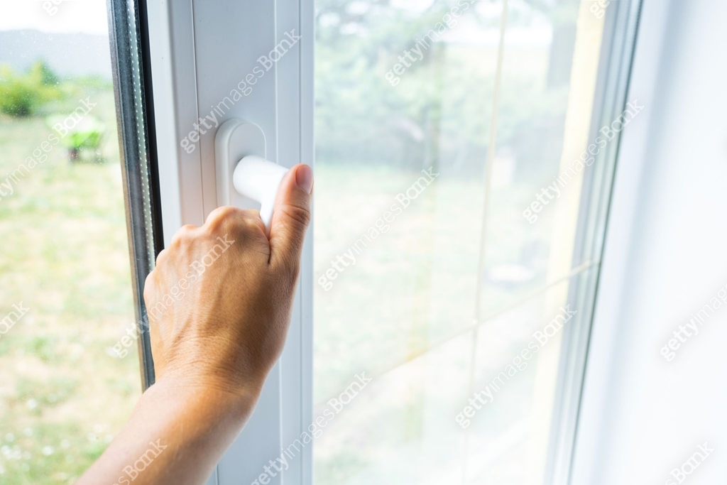 The hand holds the handle of a plastic double-glazed window, closing ...