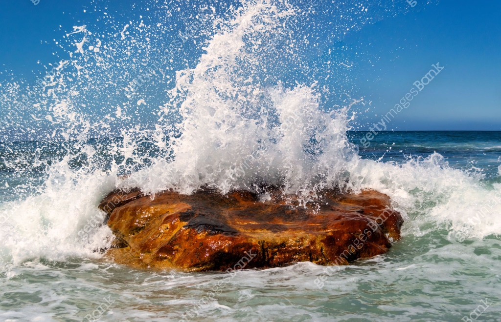 Stone Splashing wave splashing on a giant stone in the ocean, spray bubbles in the blue ...