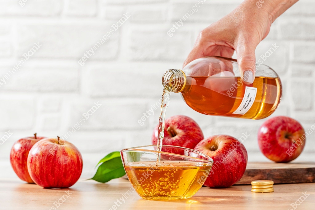 A close-up shot of a baker carefully pouring apple cider into a mixing bowl, with a few fresh apples in the background, natural lighting, close-up