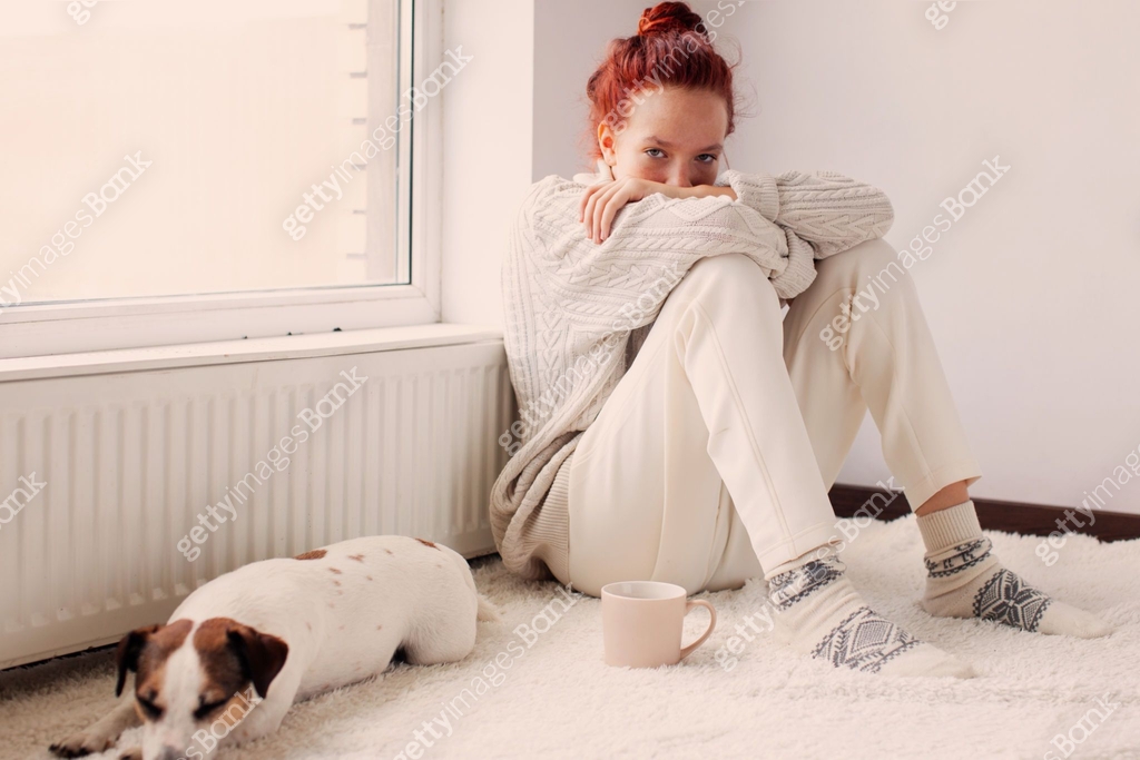 Sad young Woman sitting near radiator at home 이미지 (2181380372) - 게티이미지뱅크